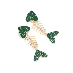 Detail of gold fishbone earrings with dark green oil drip and heart-shaped me! charm