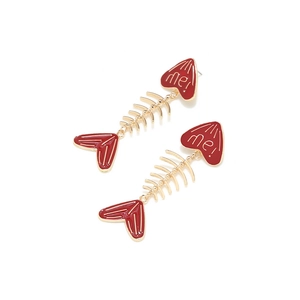 Macro detail of red enamel heart and golden fishbone pendant earrings with 'me!' text
