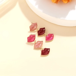 Macro detail of three layered red enamel lip charms on gold-tone earrings with glitter