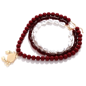 Layered multi-strand necklace featuring red beads, pearls and a golden crab pendant