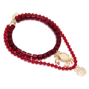 Collier artisanal à perles rouges avec pendentifs crabe et coquillage dorés sur fond blanc