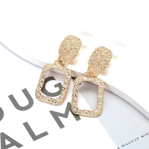 Retro geometric gold earrings with textured molten finish on a white display stand