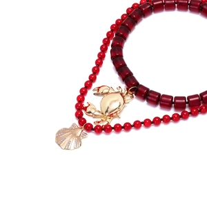 Détail de pendentifs crabe et coquillage dorés sur un collier à perles rouges superposé