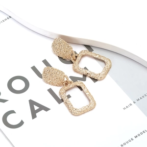 Detailed view of golden rectangle earrings with hammered texture on elegant book