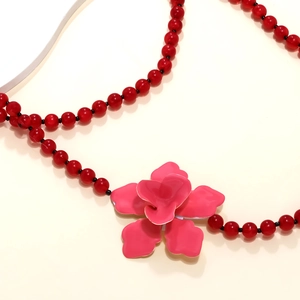 Detailaufnahme der roten Perlen mit glänzendem rosa Blumenanhänger an der Halskette
