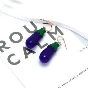 Boucles d'oreilles aubergine violette avec crochets dorés sur fond de magazine blanc pur