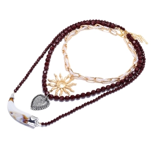 Collier bohème multicouche avec perles rouges, pendentifs soleil et cœur sur fond blanc