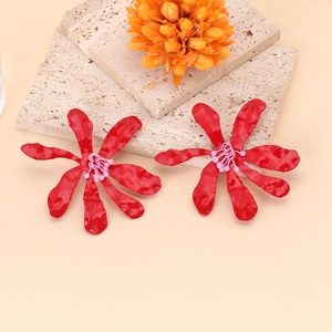 Détail macro de boucles d'oreilles fleurs rouges texturées sur un support en pierre