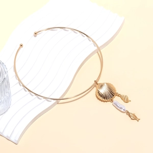 Detailed close-up of golden shell pendant and baroque pearl on minimalist choker