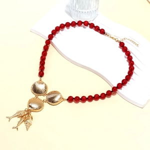 Detail of red beaded sea theme necklace featuring golden shell and tropical fish charms