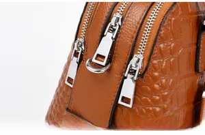 Detail of silver metallic zippers and crocodile embossed texture on brown handbag