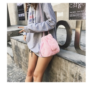 Outdoor street shot of a pink plush drawstring bucket bag with fuzzy pompom detail