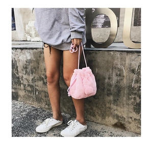 Pink faux fur drawstring bucket bag with decorative pom poms and matching strap detail