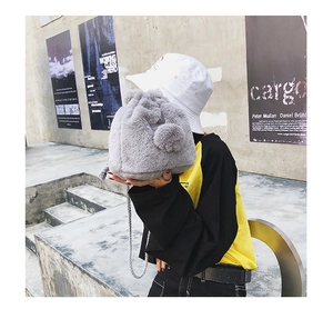 Detail of grey faux fur bucket bag with plush pom-poms and woven shoulder strap