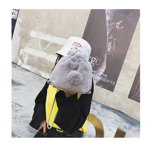 Close-up of grey faux fur bucket bag featuring plush pom-poms and woven shoulder strap