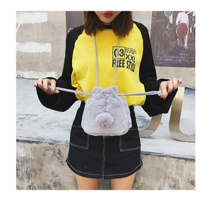 Close-up of grey plush faux fur drawstring bucket bag with decorative pom-poms on shoulder