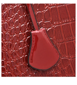 Dettaglio macro della clochette in pelle rossa con motivo a coccodrillo sulla borsa