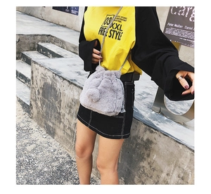 Detailed close-up of grey plush drawstring bucket bag with decorative soft pom-poms