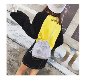Detail of gray faux fur drawstring bucket bag with pom-pom accents on model