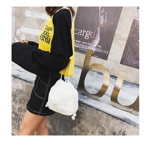 Detail view of a white fuzzy drawstring bucket bag with a pom-pom charm on a model