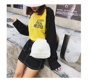 Outdoor street shot of a white faux fur bucket bag with drawstring and thin shoulder strap