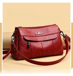 Detail view of burgundy faux leather crossbody bag with zipper and metal brand logo