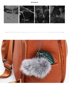 Detail of cute grey plush pendant with green leaf charm on brown leather handbag