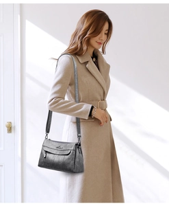 Detail of grey crossbody bag with metallic zipper and stitching on beige wool coat