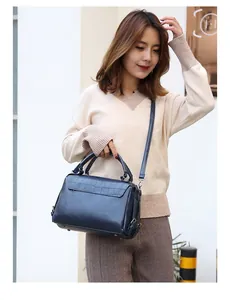 Detail of dark blue leather handbag with crocodile pattern flap on a light sweater background