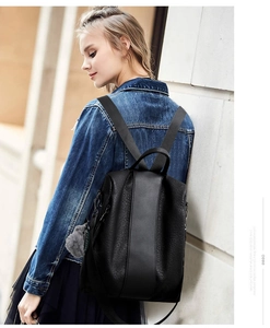 Detail of black stylish backpack for women featuring a fuzzy pom-pom and vertical strap design