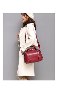 Close-up of wine red oil wax leather handbag with double buckle straps worn by a model