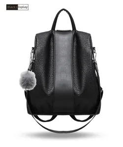 Detail view of black faux leather backpack with smooth stripes and gray pompom keychain