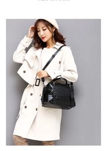 Side view of black oil wax leather handbag shown with white trench coat and boots