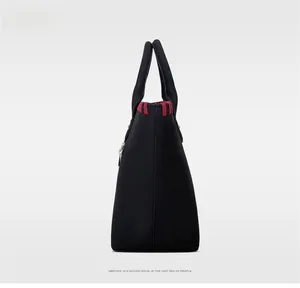 Détail du cabas noir avec coutures tissées rouges sur les bords et doubles poignées