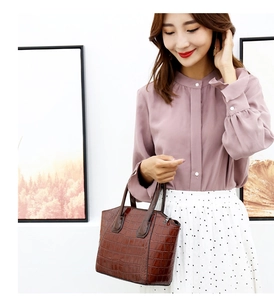 Detail of dark brown crocodile pattern handbag with elegant purple ruffle sleeve shirt