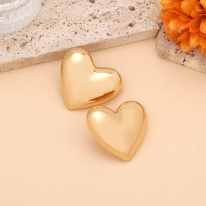 Detailed view of polished gold heart stud earrings on a textured stone aesthetic background