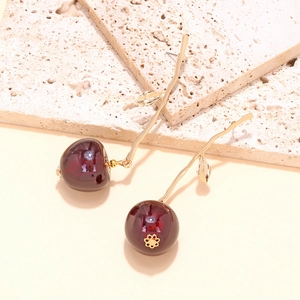 Macro shot of dark red resin cherry earrings with golden leaf details on stone background