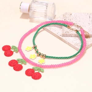 Pink beaded cherry necklace and green twisted floral choker set on beige background