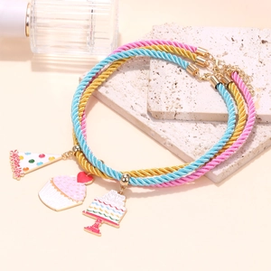 Three-piece birthday jewelry set with enamel cupcake and party hat charms on woven cords