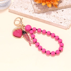 Pink beaded keychain with red heart and koi fish enamel charms on a textured stone base