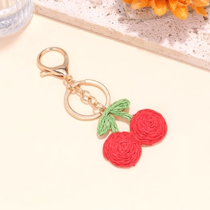 Handmade woven red cherry keychain with gold clasp on a minimalist stone background