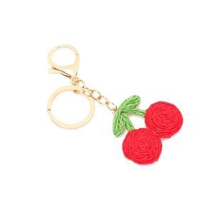 Detailed close-up of handmade crochet cherry keychain with golden metal clasp and green leaves