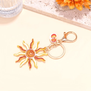 Porte-clés pendentif soleil en émail coloré avec chaîne dorée sur fond beige minimaliste