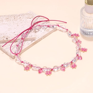 Detail of beaded necklace with pink heart charms and floral pendants on stony background