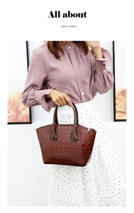 Detail of dark brown crocodile pattern handbag with dual handles held by a model