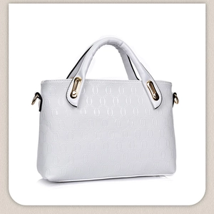 Detailed close-up of white embossed leather handbag with golden metal hardware and round pattern