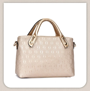 Detail of champagne gold handbag featuring embossed oval geometric texture and sturdy handles