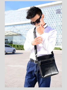 Vertical black leather shoulder bag with embossed logo worn by male model outdoors