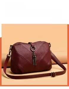 Détail du sac bandoulière bordeaux avec surpiqûres en V et pendentif à pompon doré