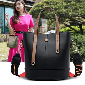 Detail of matte black leather bucket bag with brown handles and patterned wide strap